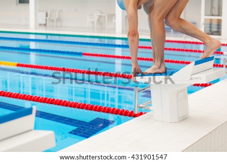 Young muscular swimmer in low position on starting block a swimming pool
