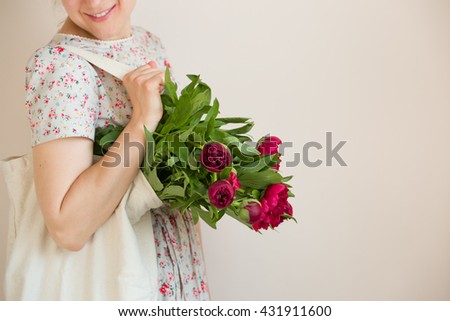 Woman holding a textile bag with beautiful bunch of red peonies. Girl's hands with bag full of peony flowers. Summer and lifestyle concept.