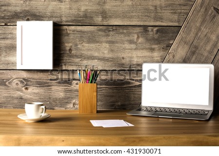 Closeup of creative wooden designer desktop with blank white laptop screen, picture frame, coffee cup and stationery items. Mock up