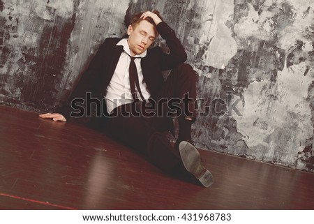 Blond man in depression sitting on the floor. Dressed in a formal classic suit. Oldshool 70s colour graded.