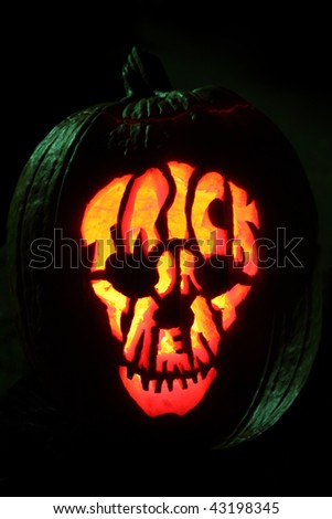 Halloween pumpkin carved into Jack O' Lantern trick or treat skull pattern under green top light.