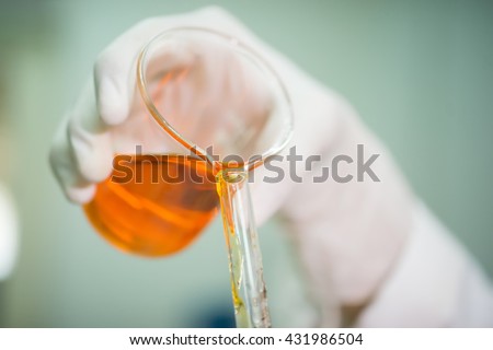 Scientist pouring orange liquid from  Erlenmeyer flask to measurement tube . Close up of hands and glassware.