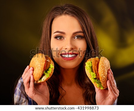 Happy girl holding two small fastfood hamburgers. Fastfood concept on green.