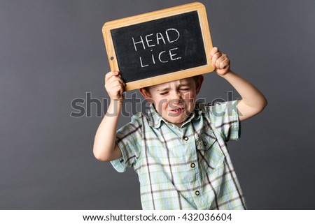 nervous 5-year old child standing and holding a stressful writing slate as a head lice protest to complain about the hair enemy, grey background studio
