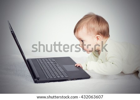 Cute baby boy with black laptop on white carpet 