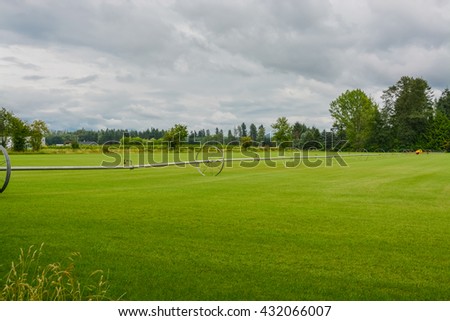 English lawn growing on a farm. Green lawn with irrigation system over the field on cloudy summer day