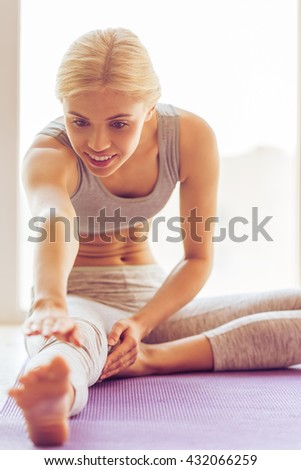 Beautiful young woman in sports wear is smiling while stretching on a yoga mat