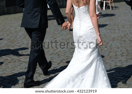 Bride and groom walking along the stony street in sunny weather shot from the back
