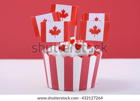 Happy Canada Day Party Cupcake with maple leaf flags on a white wood table against a red background. 