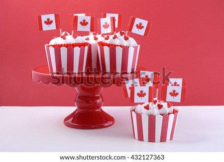 Happy Canada Day Party Cupcakes on a red cake stand with maple leaf flags on a white wood table and red background.