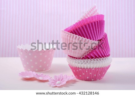 Pink cupcake paper cups on a white wood table with pink candy stripe background. 