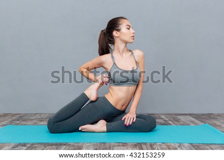 Young woman doing yoga asana Eka Pada Rajakapotasana (one legged king pigeon) isolated on grey background