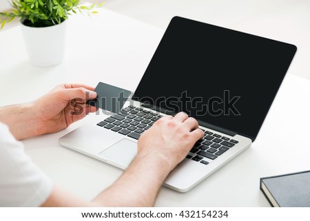 Online shopping concept with man's hands copying information from credit card to laptop with blank screen on white desktop. Mock up