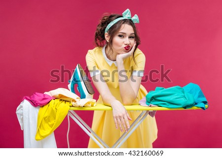 Bored sad young woman ironing clothes over pink background Royalty-Free Stock Photo #432160069