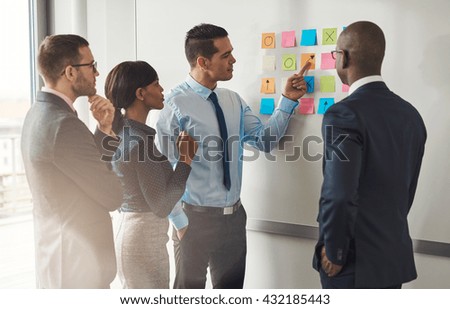 Multiracial group of colleagues discussing a business plan standing around a set of colorful memo notes stuck on the wall Royalty-Free Stock Photo #432185443