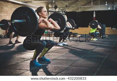 Fit young woman lifting barbells looking focused, working out in a gym with other people Royalty-Free Stock Photo #432200833
