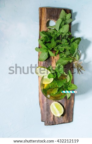 Glass of Iced green tea with lime, lemon, mint and ice cubes on wooden chopping board over light blue textured background with green textile napkin. Flat lay. With copy space