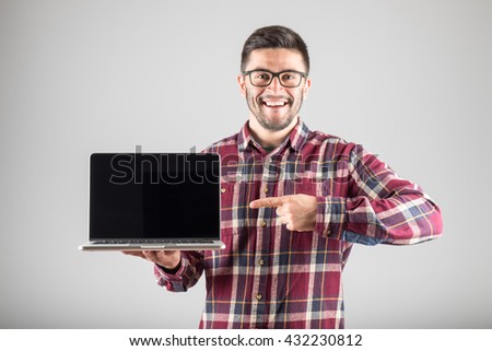 Smiling hipster pointing finger on blank laptop screen over gray background