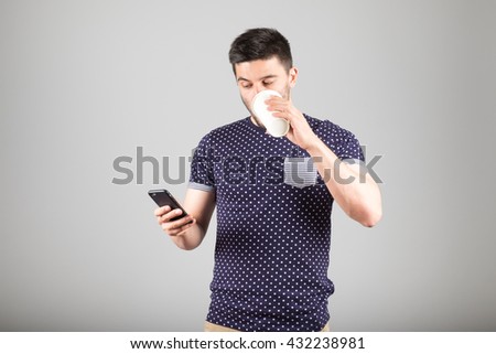 Handsome young man drinking coffee and using his smartphone isolated on gray