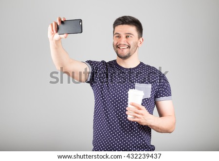 Handsome man with a coffee to go taking selfie on own phone for social networks. Isolated on gray