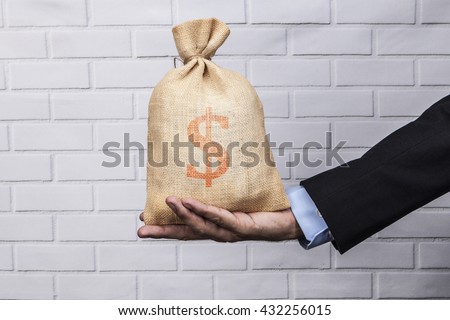 Hand holding a sack of money and white brick background