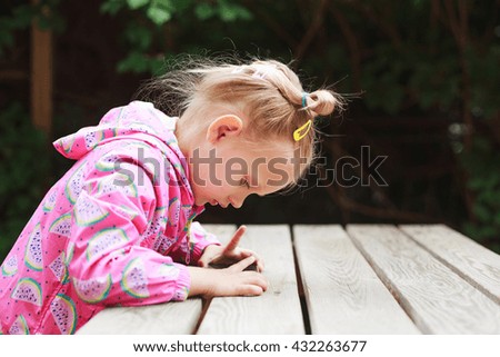 Outdoor portrait of cute blonde toddler girl using a digital tablet or smart phone.