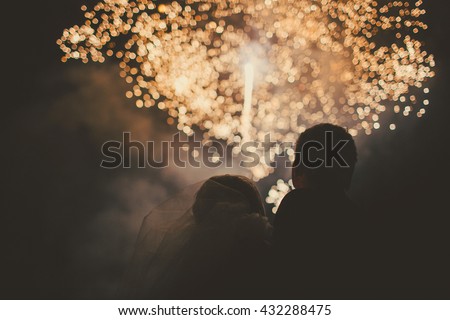 Silhouettes of bride and groom watching fireworks in night sky Royalty-Free Stock Photo #432288475