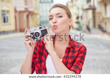 Beautiful young woman holding a camera and sending kiss to the camera.