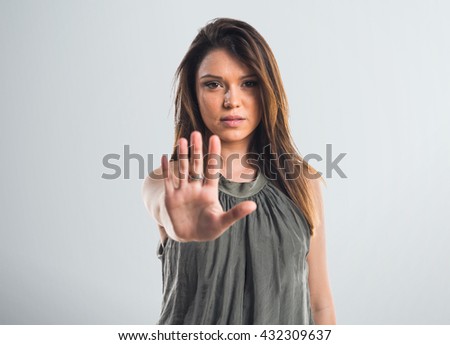 Young girl making stop sign over grey background
