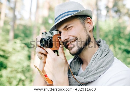 An attractive young photographer in hat takes pictures on vintage film camera on a walk in the woods