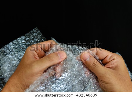hands popping the bubbles in bubble wrap on black background (selective focus) Royalty-Free Stock Photo #432340639