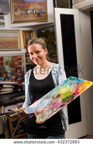 Attractive female painting in a studio holding a colorful artists palette and paintbrush in her hand