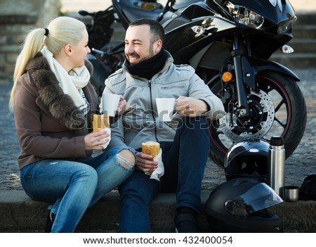 Happy adults drinking coffee and chatting near motorcycle