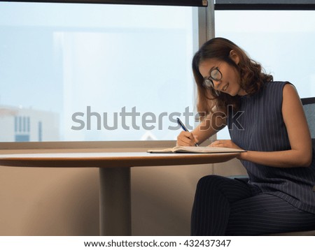 Good looking woman  writing on the desk near window with building in the background