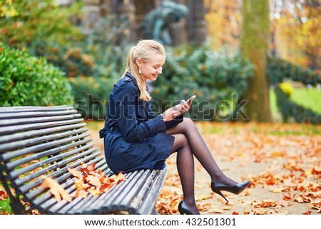 Beautiful young woman on a street of Paris on a sunny fall or spring day taking selfie with her mobile phone