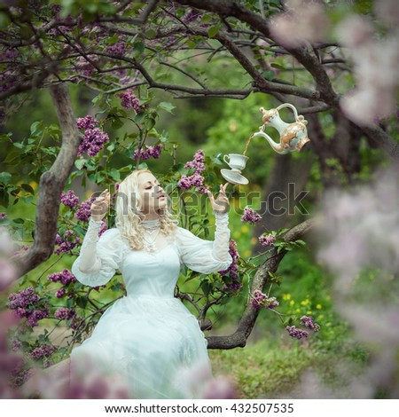 Beautiful blonde woman in blooming lilac garden. Vintage. Alice. Fairytale. Surreal tea party concept. 