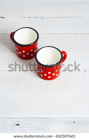 two dotted enamel mugs of milk on white wood table background