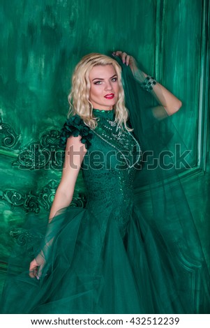 Young extravagant beautiful woman in the studio with hair and professional make-up in green vintage dress, bright red lips, blonde, thin waist, beautiful figure, fashion, magazine shooting