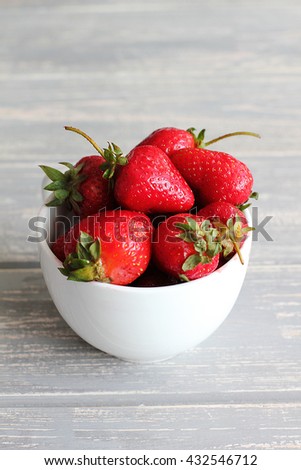 Strawberries in white cup on wooden grey desk. Stock photo.