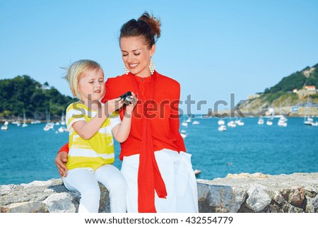 Luxury weekend with family. Happy mother and child showing photo in digital camera in front of the beautiful scenery overlooking lagoon with yachts