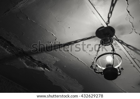 Old lamp hanging from damaged ceiling. Destruction concept. Black and white photo.
