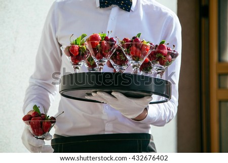 Catering service. Waiter carrying a tray of fruit cocktails with a strawberries and cherries Royalty-Free Stock Photo #432676402