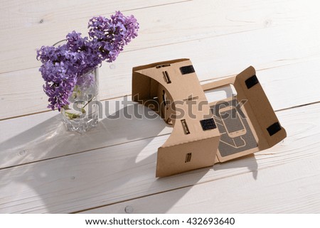 Lilac Bouquet and cardboard VR glasses on a white wooden table