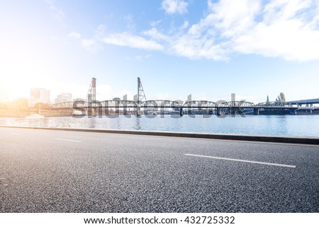 empty asphalt road near water and steel bridge in portland in blue sky