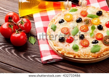 Italian pizza with cheese, tomatoes, olives and basil on wooden table