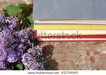 A stack of books and flowers of a lilac in the garden on wooden background. 