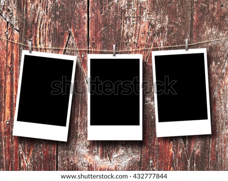 Close-up of three rectangular blank instant photo frames hanged by peg against old weathered wooden boards background