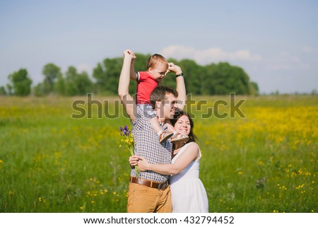 Happy family of three people hugging outside. Mother in expectation of baby. Smiling faces of woman, man and child. Baby playing with parents. Togetherness. Happy family in sunset time in countryside.