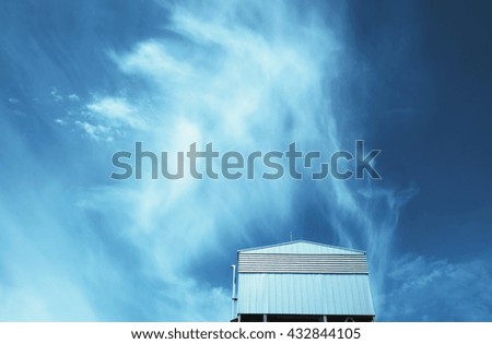 Factory/warehouse with beautiful cloud sky background. Focus on factory. Blue-green tone.