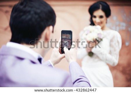 Handsome groom taking photo of beautiful bride on his phone